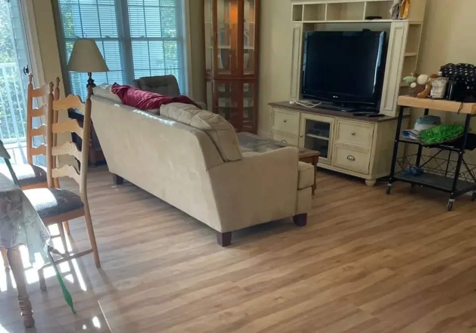 A Living Room With Newly Installed Light Brown Wood Laminate Flooring, A Couch, And A Tv Stand.