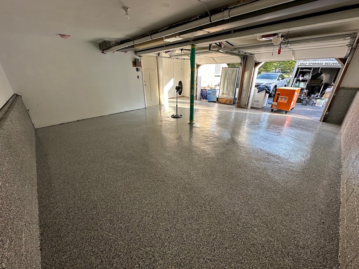 A Wide-Angle View Of A Newly Installed, Glossy Gray Epoxy Floor In A Garage With A Fan And Open Garage Door.