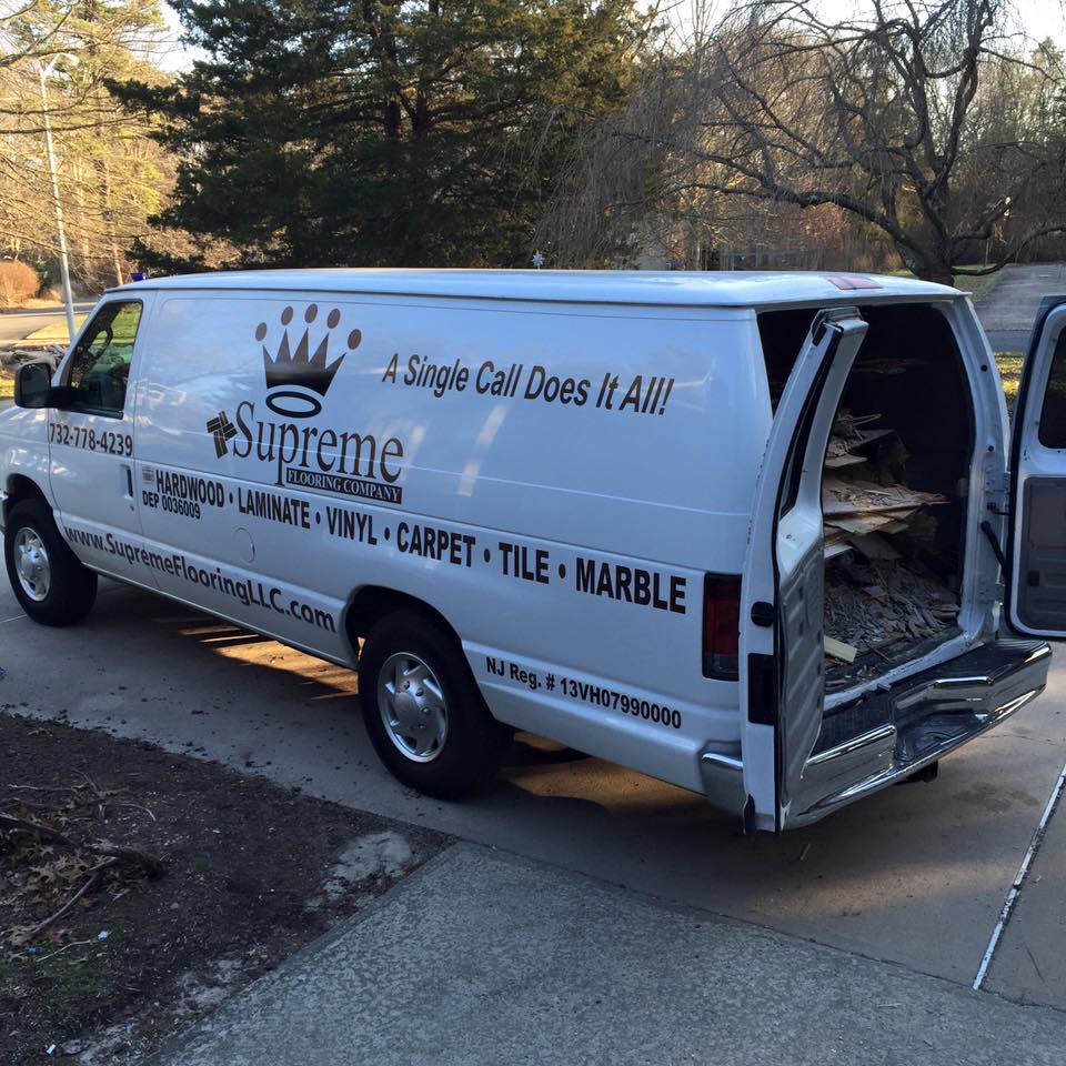 The Side View Of A White Supreme Flooring Company Van Parked On A Paved Driveway.