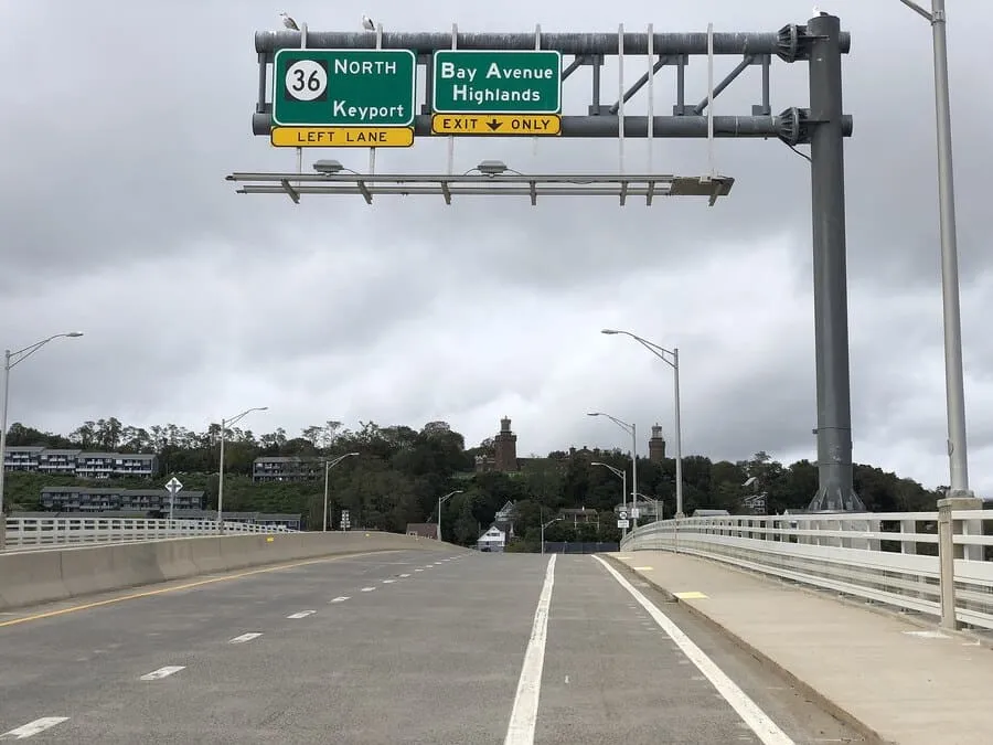 A View From A Bridge Showing Overhead Signs For Route 36 North To Keyport And An Exit For Bay Avenue Highlands. In The Background, There Is A Treeline With Some Buildings.