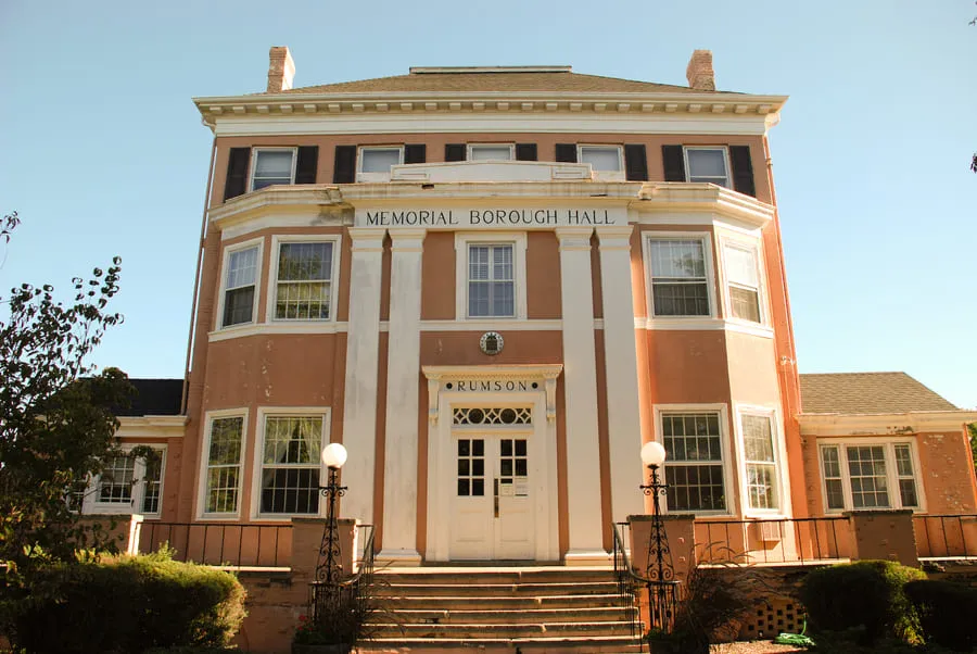A Front View Of A Historic, Peach-Colored Building With The Words &Quot;Memorial Borough Hall&Quot; And &Quot;Rumson&Quot; On The Front, And Large White Columns Framing The Entrance.